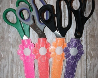 Könnte beinhalten: Vier Scheren mit dekorativen, blumenförmigen Haltern. Die Halter sind rosa, orange, pfirsichfarben und lila.