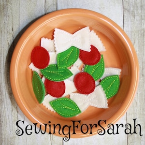 May include: A bowl of felt food, including red and green felt pieces shaped like tomatoes and basil leaves, and white felt pieces shaped like bowtie pasta. The bowl is on a wooden surface. SewingForSarah is written in the bottom of the image.