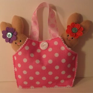 May include: Pink polka dot fabric tote bag with two brown bunny plushes with purple and red flowers. The bunnies have embroidered faces.
