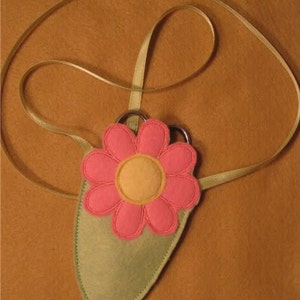 May include: A green felt flower-shaped pouch with a pink flower and yellow center. The pouch has a long, thin, light brown ribbon attached to it.