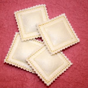 May include: Four white square ravioli pasta with a gold-colored decorative edge.