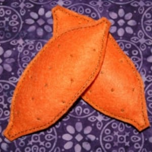 May include: Two orange felt sweet potatoes, sewn together with a brown thread. The felt is textured to resemble the skin of a sweet potato.
