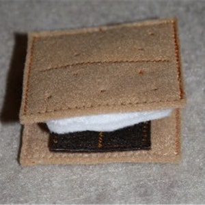 May include: A felt s'more with a graham cracker base, a marshmallow layer, and a chocolate square.