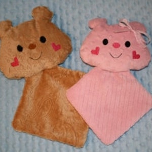Op de afbeelding: Twee pluche knuffels in de vorm van dierenkoppen, een bruine en een roze, met geborduurde hartjes en lachende gezichten.