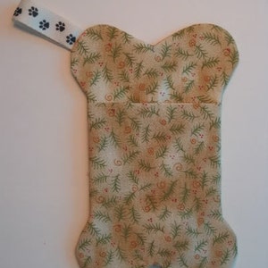 May include: A bone-shaped fabric stocking with a green and brown floral pattern. The stocking has a white fabric loop with black paw prints.