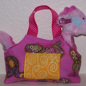 May include: Pink and yellow fabric tote bag with a whimsical design. The bag has a large pocket on the front and a pink plush toy peeking out of the top.