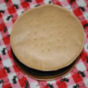 May include: A round, tan-colored cookie jar with a black elastic band around the middle. The jar has a textured surface with small holes.