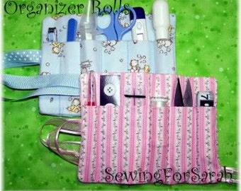 May include: Two fabric organizer rolls, one blue with a white bear print and one pink with white stripes. Both rolls have multiple pockets for holding small items like scissors, tweezers, and needles. The blue roll has a ribbon tie and the pink roll has a pink ribbon tie. The text "SewingForSarah" is printed on the pink roll.