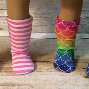May include: Two pairs of doll socks. One pair is pink and white striped. The other pair is rainbow mermaid scale print.