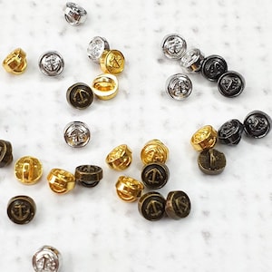 Op de afbeelding: Assortiment van kleine metalen knopen in goud, zilver en zwart met een ankerontwerp.