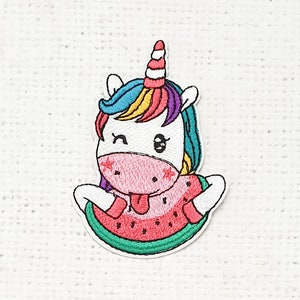 Può includere: Toppa ricamata con un unicorno stravagante con criniera e corno colorati. L'unicorno è posizionato in una fetta di anguria, con una combinazione di colori rosa e rosso. La toppa ha un bordo bianco.