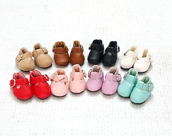 May include: A collection of 12 miniature doll shoes in various colours, including pink, red, blue, white, and brown. The shoes have a strap across the top and a buckle fastening.