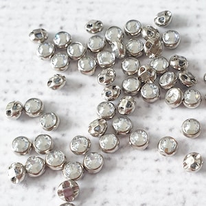 Peut inclure: Un grand nombre de strass en cristal transparent avec des montures argentées. Les strass sont éparpillés sur une surface blanche.