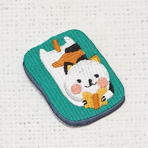 May include: Embroidered iron-on patch featuring two white cats reading a book on a green background.