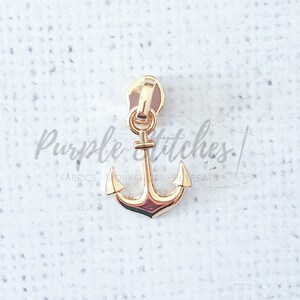 May include: Gold anchor zipper pull. The anchor is a nautical design with a classic shape.