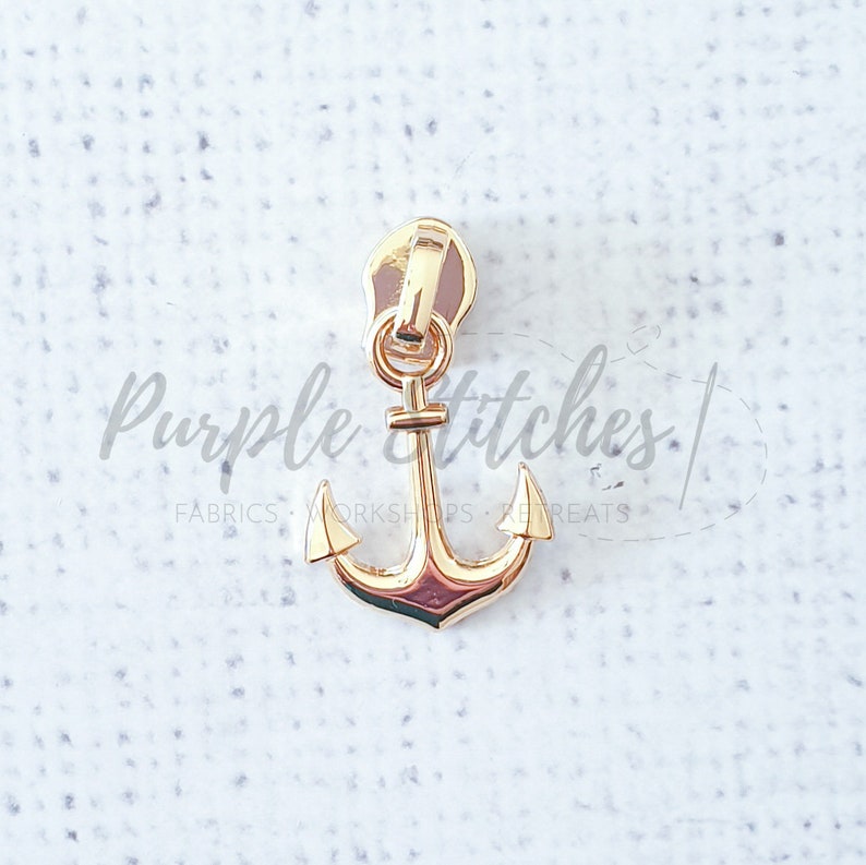 May include: Gold anchor zipper pull. The anchor is a nautical design with a classic shape.
