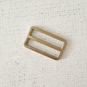 Pu&ograve; includere: Una fibbia in metallo dorato con due fessure parallele. La fibbia &egrave; di forma rettangolare e ha una finitura liscia e lucida.