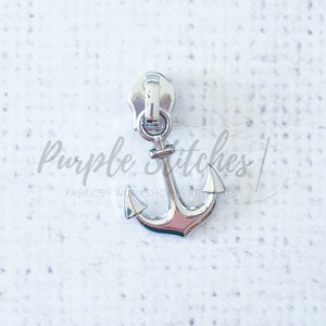 May include: Silver zipper pull with an anchor design. The anchor is a nautical theme.