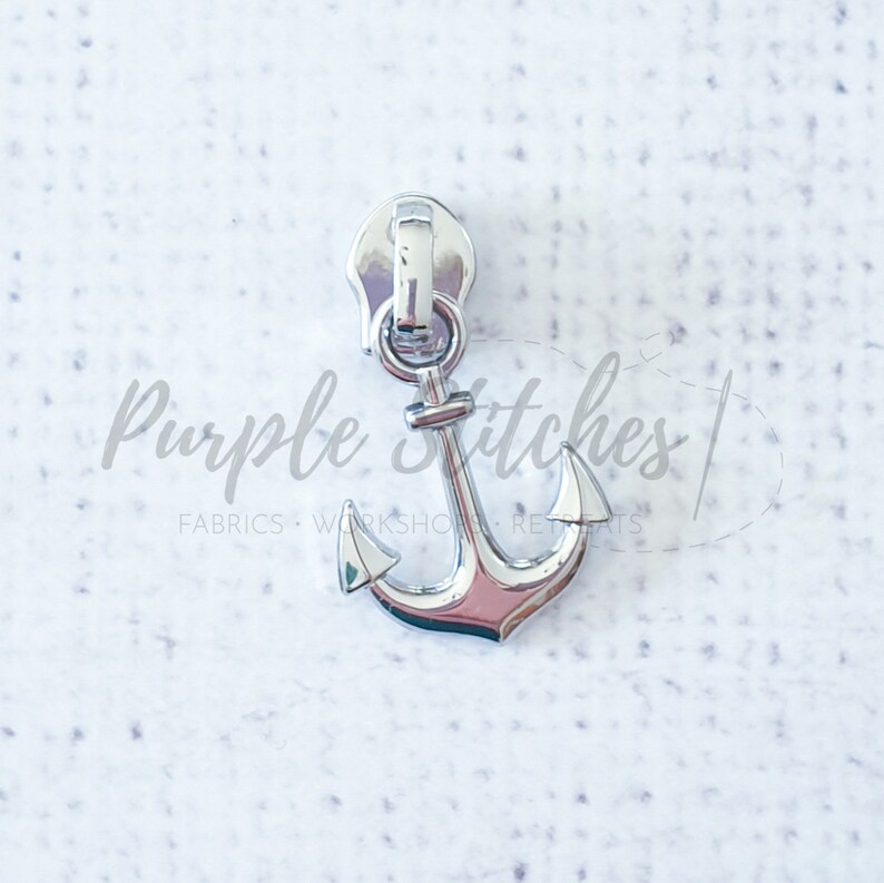 May include: Silver zipper pull with an anchor design. The anchor is a nautical theme.