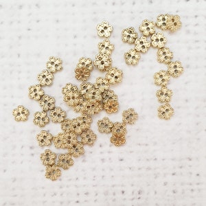 May include: A scattering of gold metal flower-shaped embellishments on a white surface.