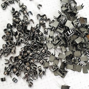 May include: A large quantity of black metal zipper pulls and slider heads. The zipper pulls are in the shape of a loop with a small ball at the end. The slider heads are rectangular with a small hole in the center.