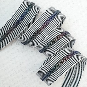 May include: Black and white striped ribbon with a iridescent black zipper tape. The ribbon is folded and twisted into a decorative display.