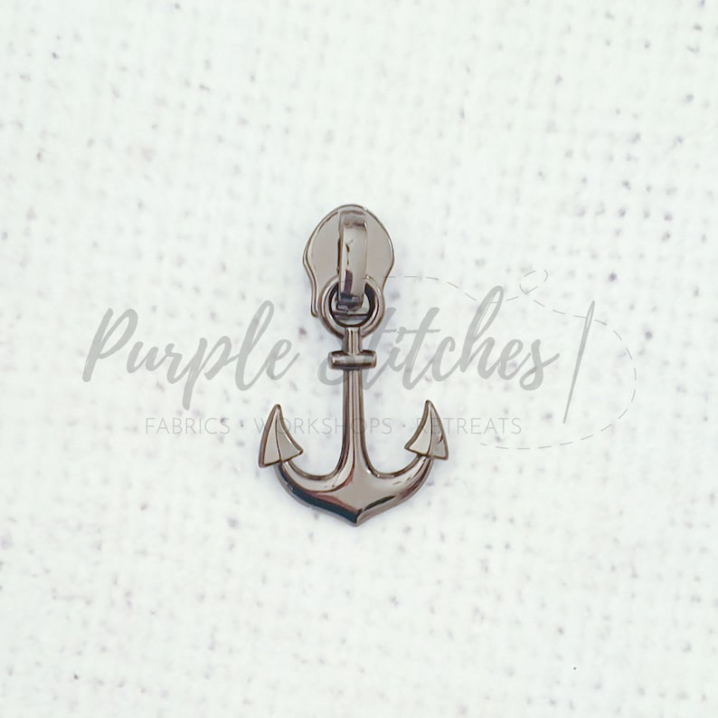 May include: A silver metal zipper pull in the shape of an anchor. The anchor has a loop at the top for attaching to a zipper.