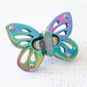May include: A rainbow iridescent butterfly-shaped metal clasp. The clasp is designed to be used for attaching straps or belts.