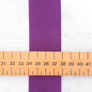 Pu&ograve; includere: Nastro elastico viola misurato contro un righello di legno con i numeri da 31 a 41. Il nastro &egrave; largo circa 2,5 cm.