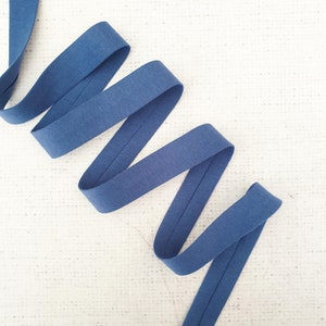 May include: A blue cotton bias tape, folded and twisted into a spiral shape, against a white textured background.