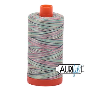 May include: A spool of Aurifil thread in a multi-coloured variegated pattern with shades of pink, blue, green, and beige. The spool is orange and has the Aurifil logo on the side.