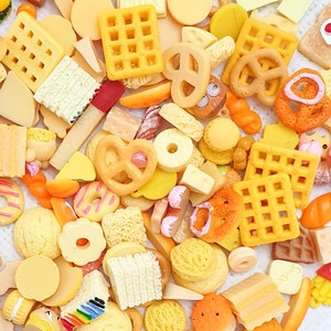 May include: A collection of miniature yellow and orange food items, including pretzels, waffles, and other snacks. The items are made of plastic or resin and are designed to look like real food.
