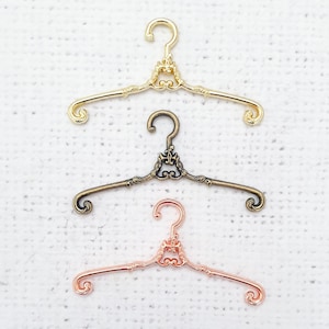 Peut inclure: Trois cintres décoratifs en or, bronze et or rose. Chaque cintre présente un design orné unique avec un sommet enroulé et un centre en forme de cœur.