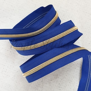 May include: A close-up of a blue zipper with a gold metal zipper pull. The zipper is coiled and ready to be used for sewing projects.