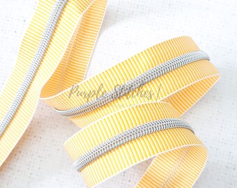 May include: A close-up of yellow and silver zipper tape. The tape has a striped pattern and is made of a durable material.