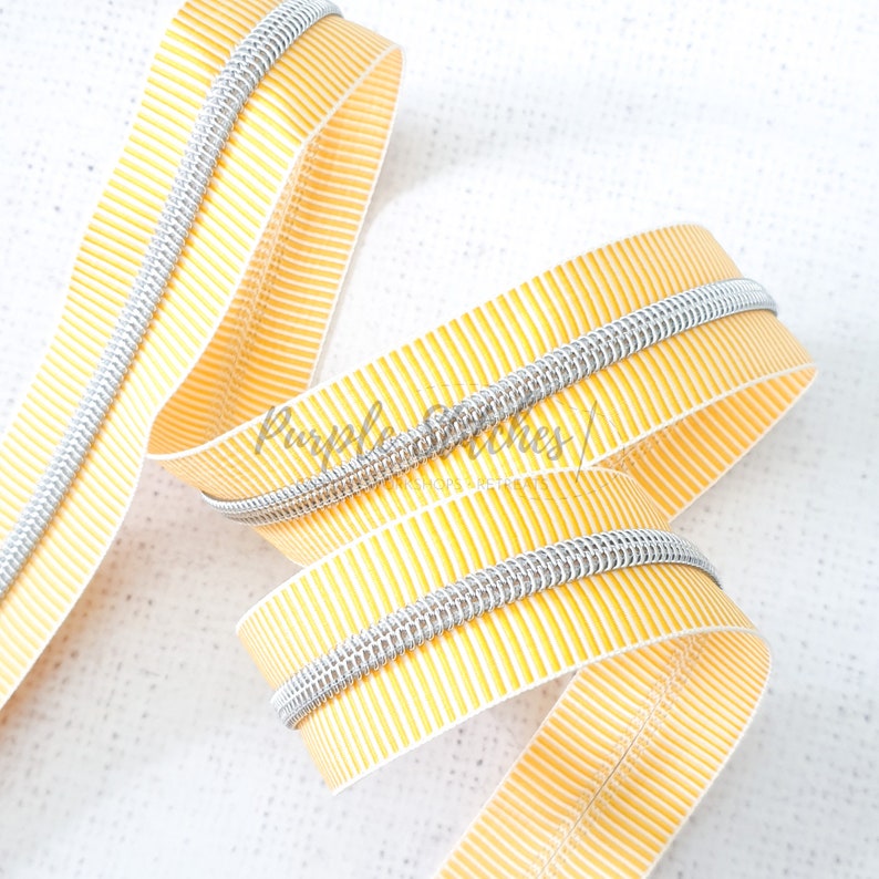 May include: A close-up of yellow and silver zipper tape. The tape has a striped pattern and is made of a durable material.