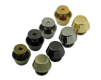 Könnte beinhalten: Sortiment von sieben metallenen Schraubnieten in verschiedenen Ausführungen, darunter Gold, Silber und Schwarz. Die Nieten sind rund mit einer leicht gewölbten Oberseite und einer Schraubbasis.