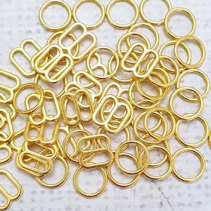 Puede incluir: Primer plano de un montón de anillas de salto de metal dorado. Las anillas son de varios tamaños y formas, algunas son anillas simples y otras son anillas dobles.