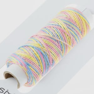May include: A spool of colorful thread in pastel shades of yellow, pink, and blue. The thread is tightly wound around a cardboard core, creating a cylindrical shape. The thread is likely used for sewing or crafting projects.