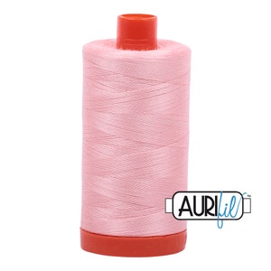 Pode incluir: Uma bobina de fio Aurifil rosa com parte superior e inferior vermelhas. A bobina é etiquetada com "Aurifil" em texto azul.