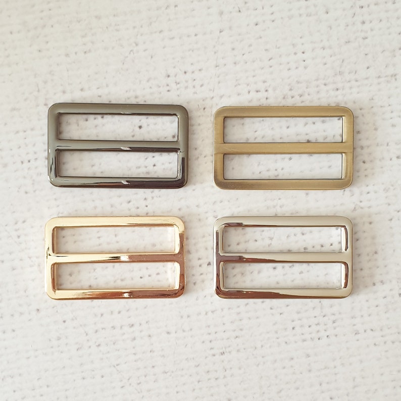 Pu&ograve; includere: Quattro fibbie scorrevoli in metallo in diverse finiture: argento, oro, nichel nero e ottone anticato. Ogni fibbia ha due barre orizzontali.