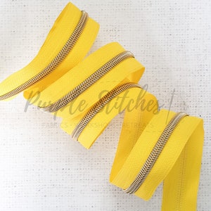 May include: A bright yellow zipper with a gold metal slider. The zipper is coiled and ready to be used in a sewing project.