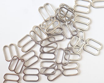 May include: A pile of silver metal slider buckles, also known as D-rings, for sewing projects. These are commonly used for straps, bags, and clothing.