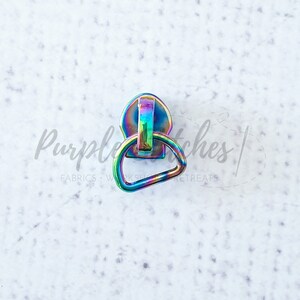 May include: A rainbow iridescent zipper pull with a D-ring. The zipper pull is made of metal and has a shiny finish.
