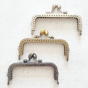 May include: Three metal purse frames in different sizes. The frames are silver, gold, and bronze. The frames are ornate with decorative details.