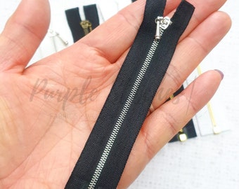 May include: A black zipper with a silver slider. The zipper is 5 inches long and is held in a hand.