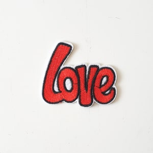 May include: Embroidered patch with the word "love" in red, outlined in black, and a white border. The patch has a cursive font style and is likely for clothing or accessories.