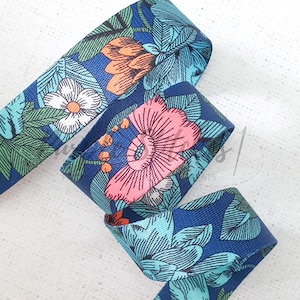 May include: A length of floral ribbon in a deep blue colour. The ribbon features a repeating pattern of stylized flowers in shades of pink, orange, white, and teal, with green leaves. The ribbon is folded over itself.