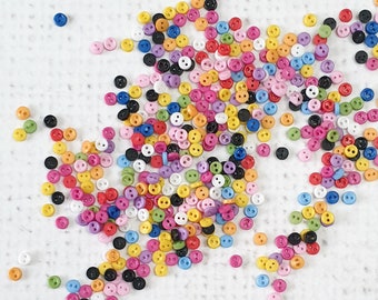 May include: A large assortment of colorful plastic buttons in various shapes and sizes. The buttons are scattered on a white surface.