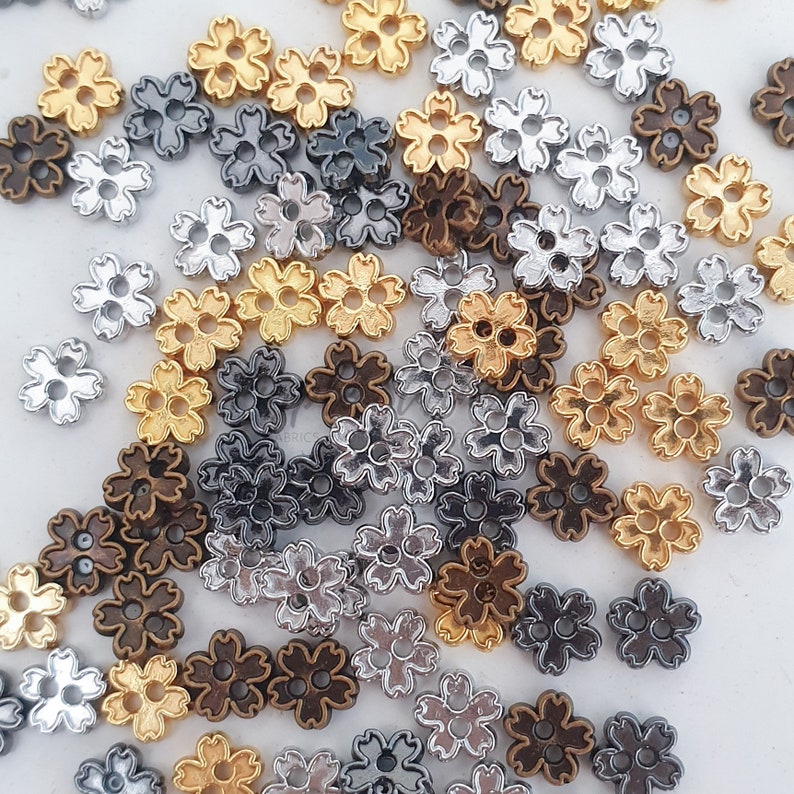 May include: Assortment of small metal flower charms in silver, gold, and bronze colors. The charms have a five-petal flower design.
